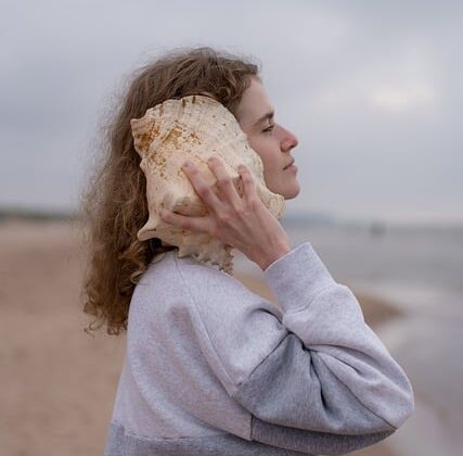 Hören: Frau mit großer Strandmuschel am Ohr